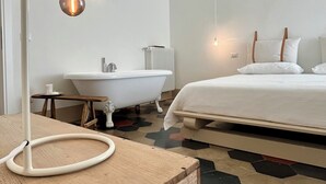Een moderne hotelkamer met een badkuip, een houten nachtkastje en een bed met wit beddegoed.