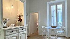 Een kamer met een wit kastje, een tafel met twee stoelen, een raam met uitzicht en een plafond met zichtbare balken.