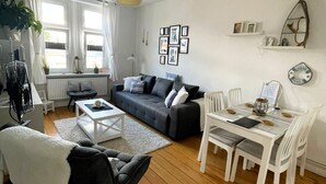 Una sala moderna con un sofá gris, una mesa de centro blanca y una zona de comedor con una mesa y sillas blancas.