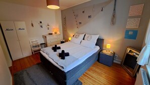 Un dormitorio ordenado con cama, mesitas de noche, un armario y una pared con diversos objetos y adornos.