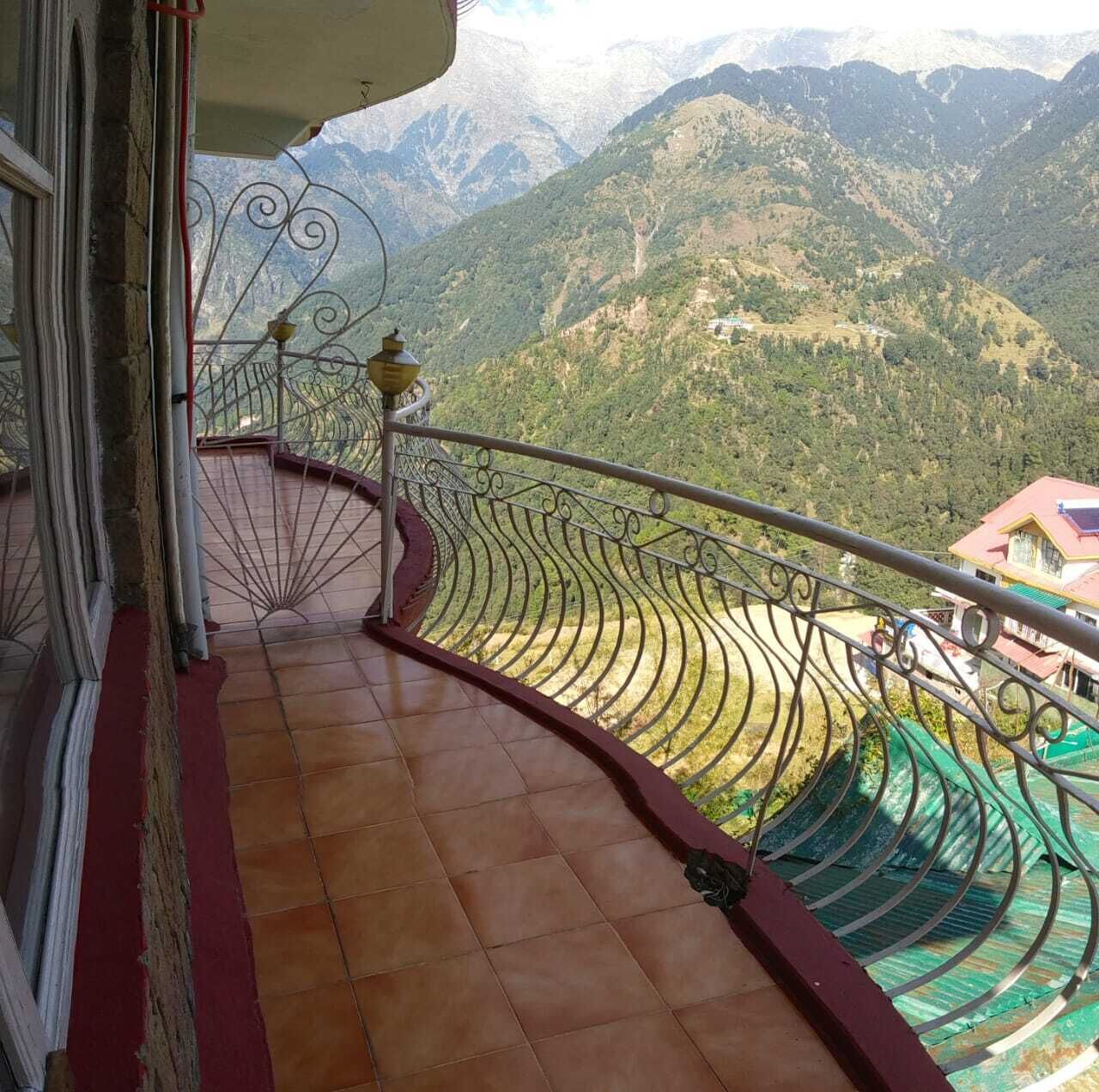 A balcony with a curved metal railing and a tiled floor, overlooking a mountainous landscape.