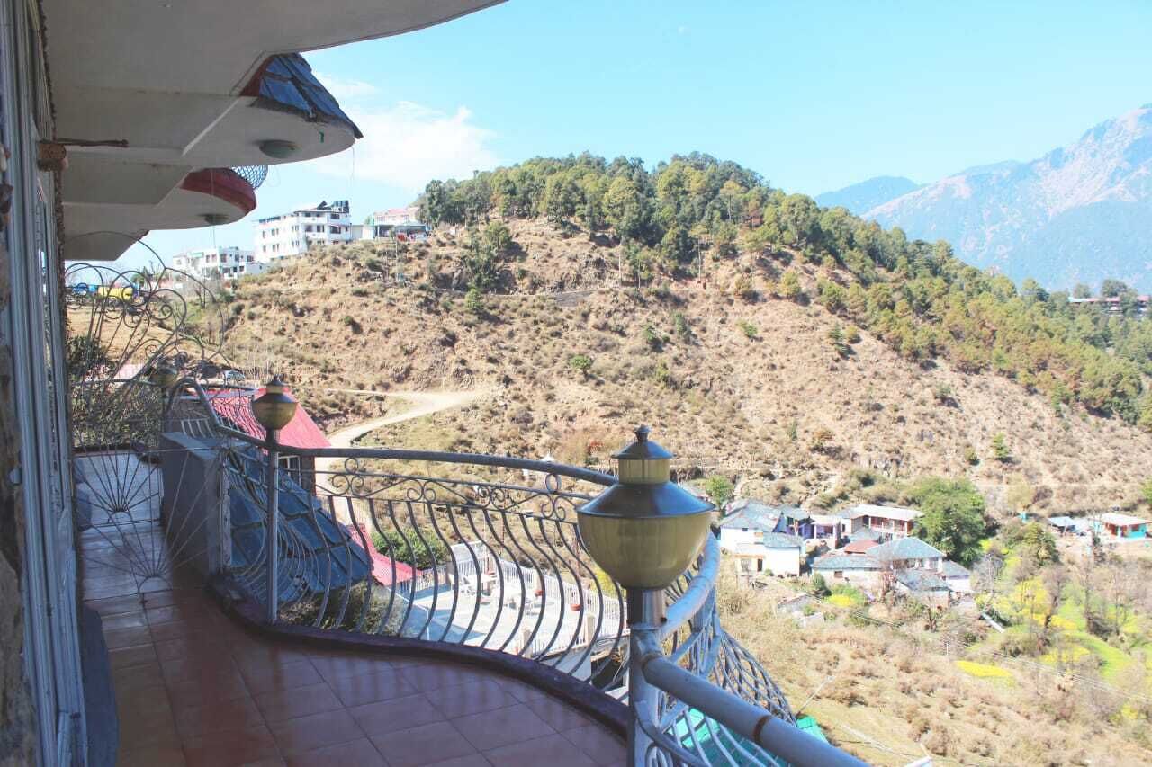 A balcony with a view of a hilly landscape, a metal railing, and a building in the background.