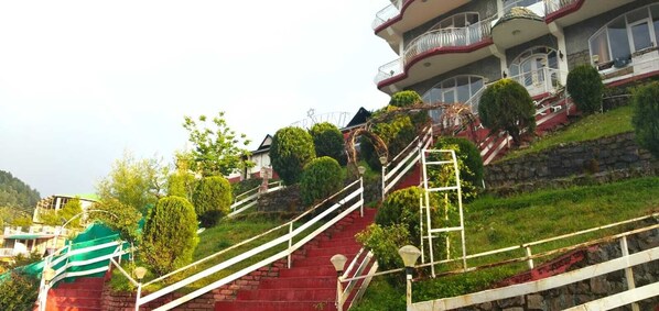 A multi-story building with a red staircase leading up to a balcony. - Hotel Victoriya palace (Dharamshala)