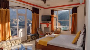 Habitación de hotel con cama, televisión, balcón y vistas a montañas.