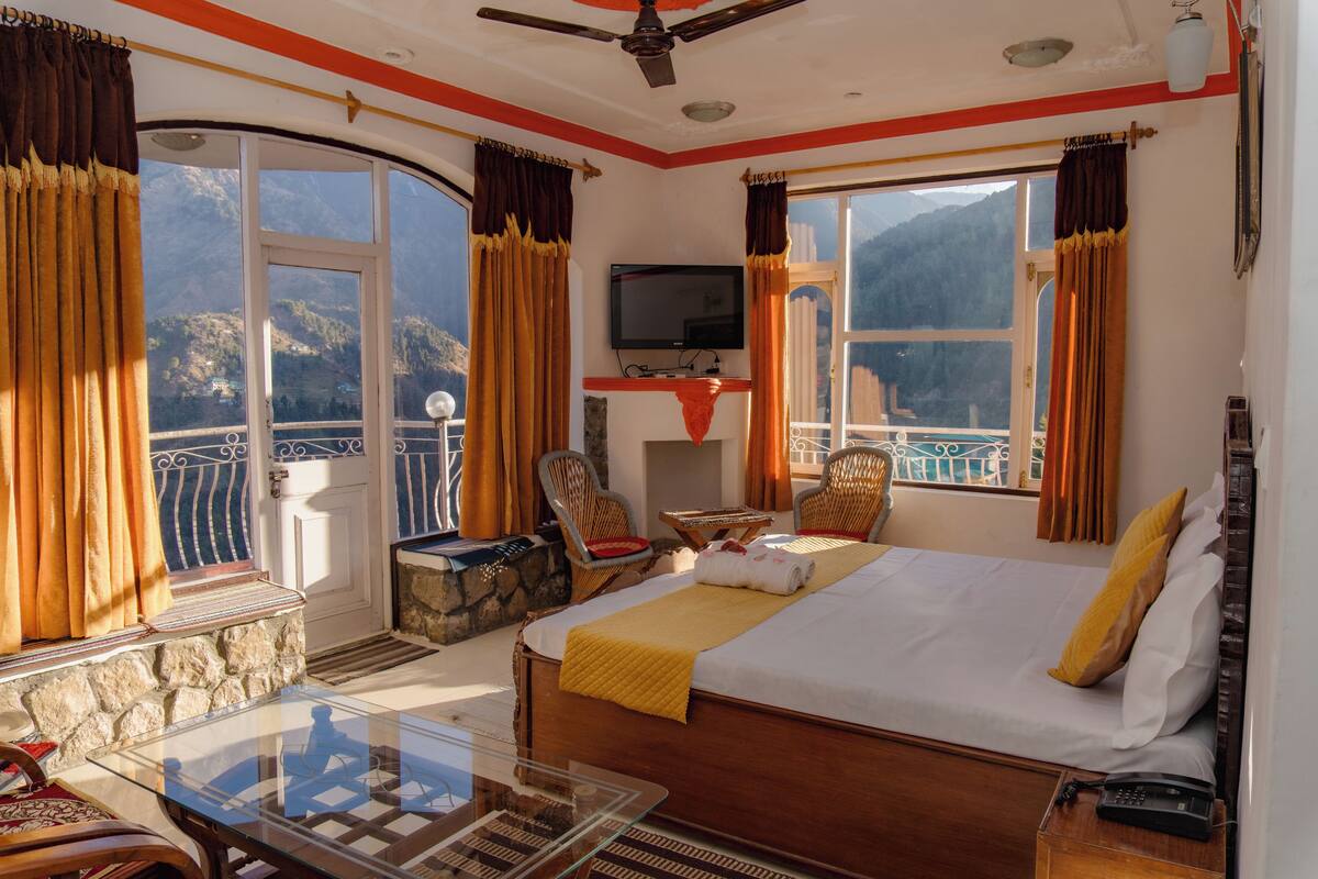 A hotel room with a bed, a TV, a balcony, and a view of mountains.