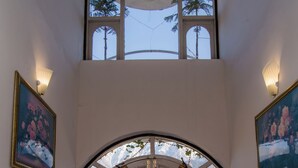 Un vestíbulo de doble altura con una puerta blanca, plantas en macetas y cuadros en las paredes.