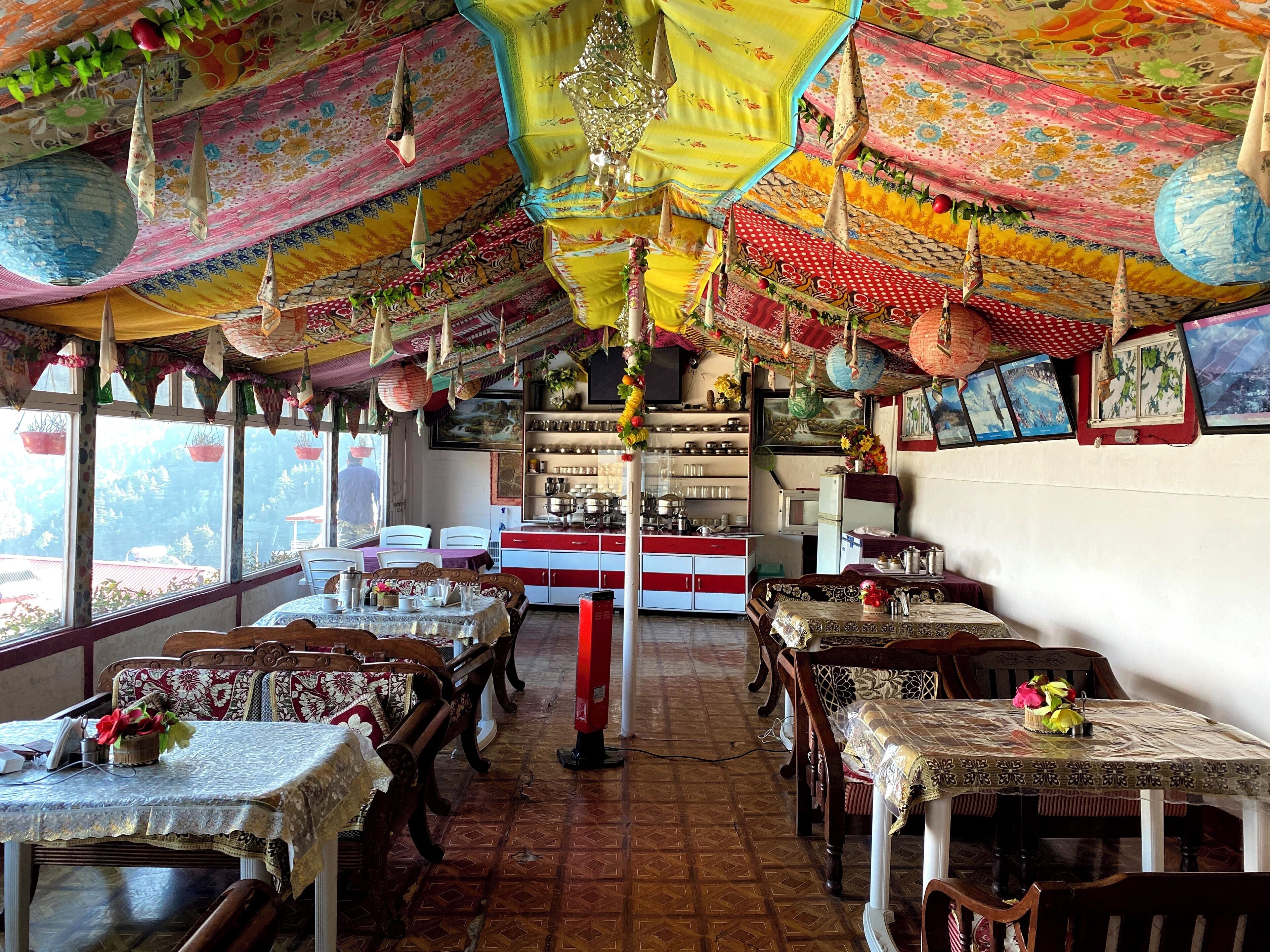 A restaurant with traditional decor, including hanging lanterns and patterned ceiling. Tables are set with tablecloths and chairs.