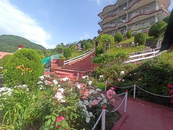 Un edificio de varios pisos con balcones, rodeado de jardines cuidados y una escalera que lo lleva al acceso.