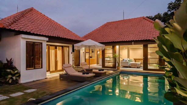 Ein zweistöckiges Haus mit Swimmingpool, Sitzgelegenheit im Freien und einem gut beleuchteten Innenraum.