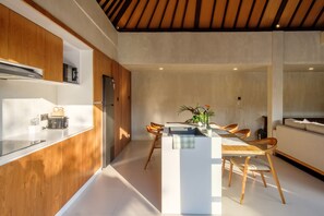 A modern kitchen with wooden cabinetry, a central island with seating, and a dining area with chairs. - Madeira Casa Canggu Bali (Canggu)