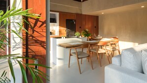 Eine moderne Küche mit Holzakzenten, ein Essbereich mit weißem Tisch und Stühlen sowie ein Wohnbereich mit einem weißen Sofa.