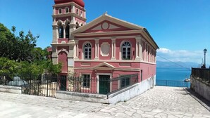 A building with a red and white facade, a bell tower, and a view of the sea. - Ideally Situated Corfu Old Town Family Retreat (Kerkira)