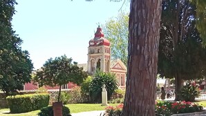 A courtyard with a large tree, a statue, and a building with a red dome in the background. - Ideally Situated Corfu Old Town Family Retreat (Kerkira)