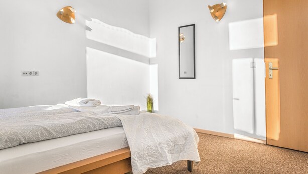 A modern bedroom with a bed, bedside lamps, a mirror, and a door. - Cozy 2BR Apt Next to Millennium Tower (Vienna)