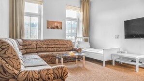 A modern living room with a patterned sofa, a glass coffee table, a white desk, and a flat-screen TV mounted on the wall. - Cozy 2BR Apt Next to Millennium Tower (Vienna)