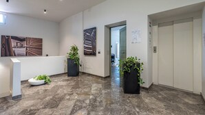 Een moderne lobby met marmeren vloeren, zwarte plantenbakken met groene planten en kunstwerken aan de muren.