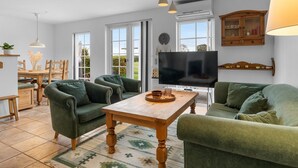 Ein großzügiges Wohnzimmer mit grünen Sofas, einem Holztisch und einem Flachbildfernseher.