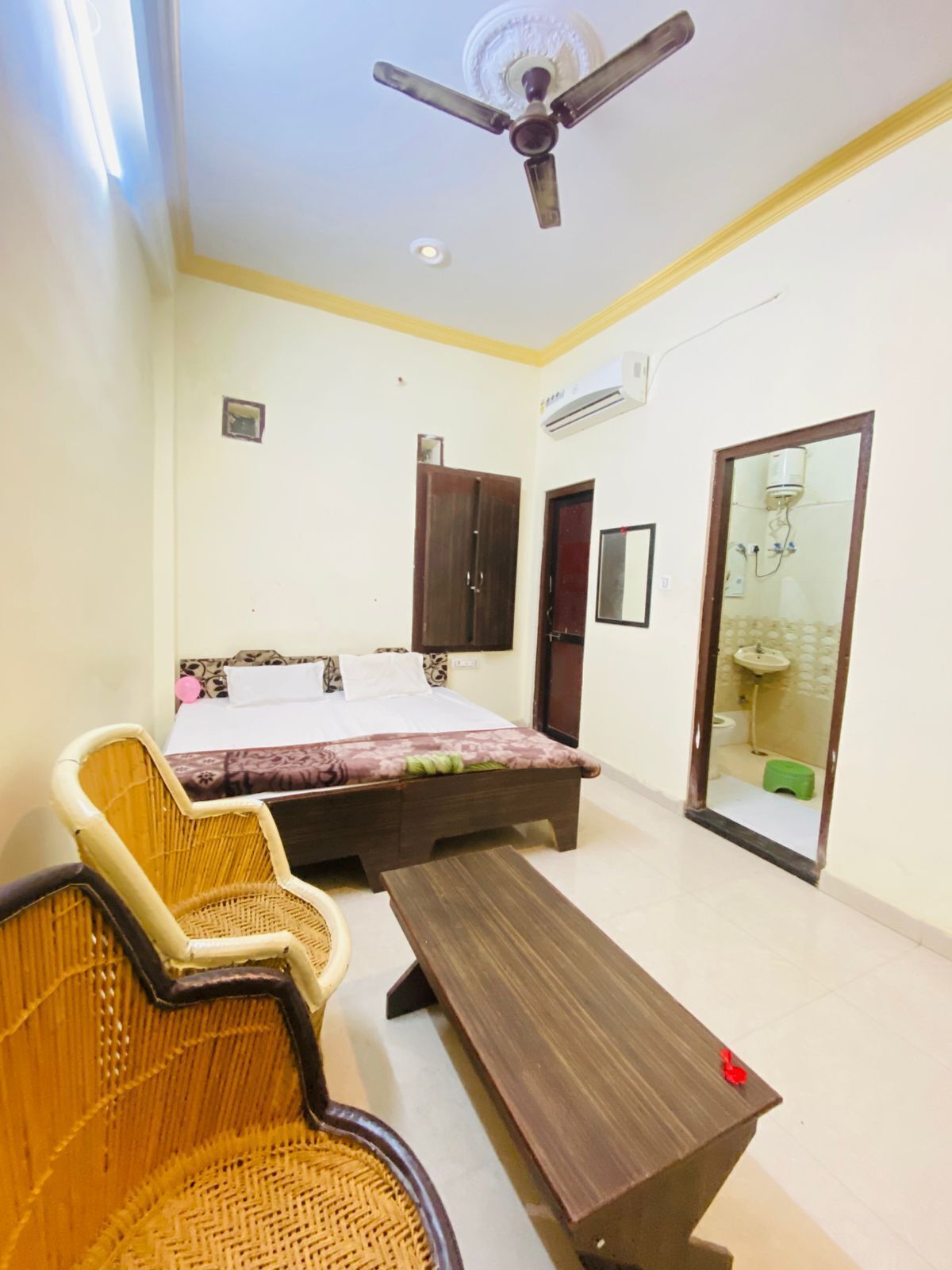 A bedroom with a bed, a chair, a table, an air conditioning unit, and a ceiling fan.