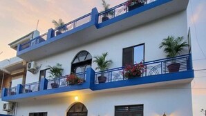 Un immeuble de deux étages doté de balcons, de plantes en pot et d’un scooter garé devant.