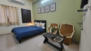 Une chambre à coucher comprenant un lit, une table de chevet avec un vase, deux fauteuils en osier et un climatiseur fixé au mur.