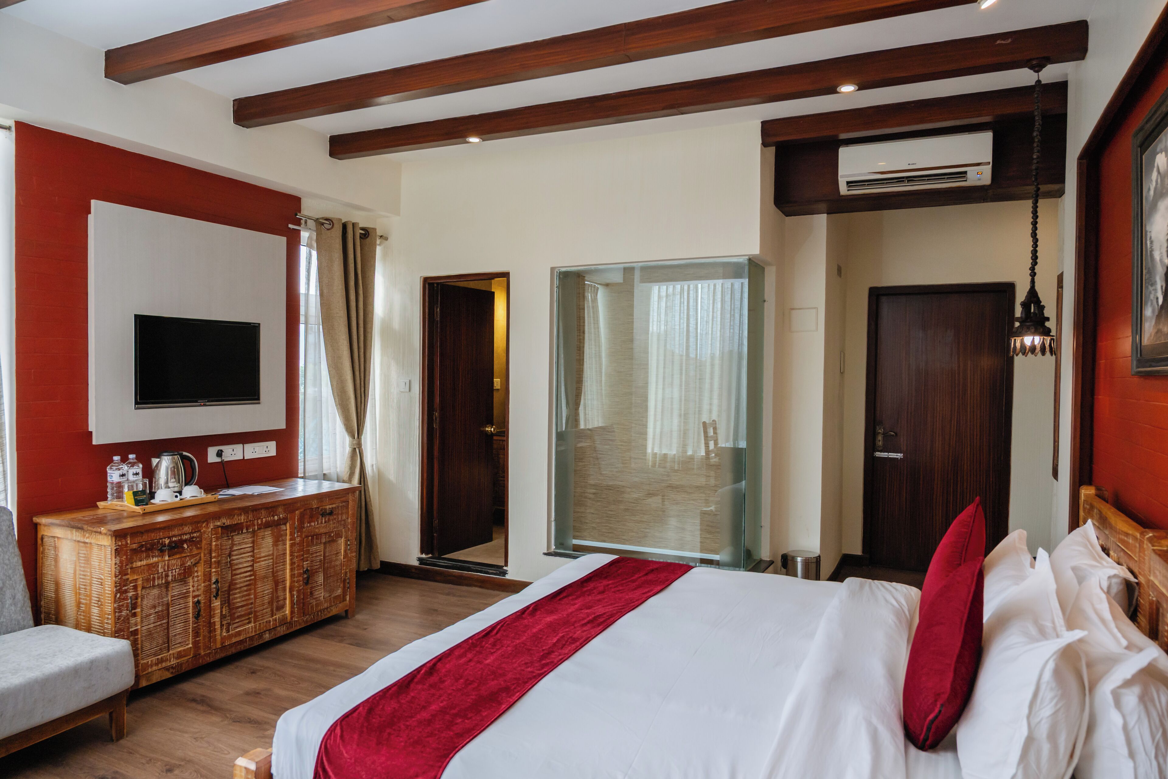 Habitación de hotel con cama, televisión, cómoda de madera y puerta que da a un balcón.