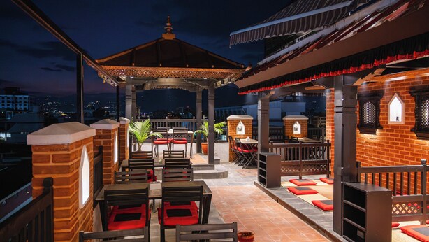 An outdoor patio with seating and a gazebo, featuring brick walls and wooden furniture. - Evara Boutique Hotel (Kathmandu)