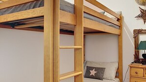 Una cama litera con escalera, un aparador, un espejo y una decoración de cabeza de venado en una habitación con suelo de baldosas.