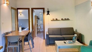 A living room with a sofa, a coffee table, a dining table with chairs, and a kitchen area visible through an open door. - Mini villa 3 private pool. (Propriano)