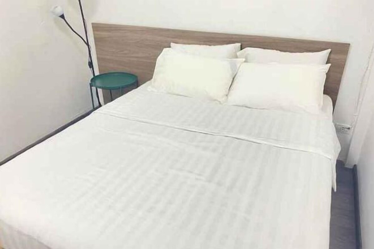 A bed with white bedding, a wooden headboard, and a green side table.