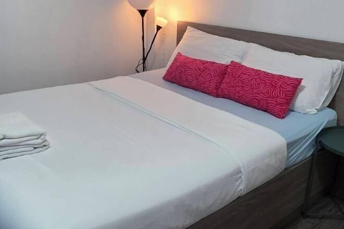 A neatly made bed with white and pink patterned pillows, a folded white towel, and a bedside lamp.