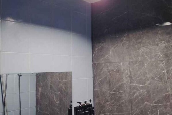 A bathroom with a marble wall, a shower area, and a sink with toiletries. - ONEWAY GUEST HOUSE BKK (Bangkok)