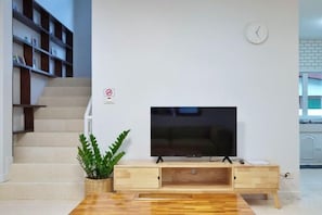 Un salon moderne avec un téléviseur à écran plat posé sur un meuble en bois, un escalier sur la gauche et une horloge au mur.