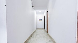 Un pasillo estrecho de paredes blancas y suelo de mármol, que conduce a una puerta al final.
