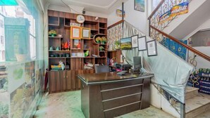 Un mostrador de recepción con una computadora, una estantería de madera y una escalera con barandillas decorativas.