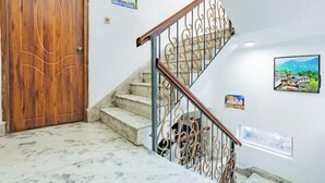 Una puerta de madera, una escalera de mármol con barandillas de metal ornamentadas y una pared con cuadros enmarcados.