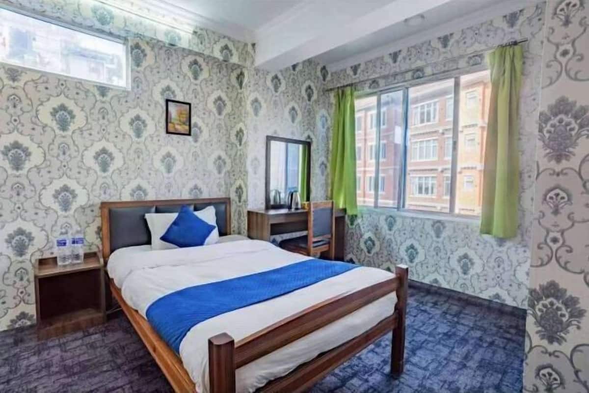 A hotel room with a bed, a nightstand, a mirror, and a window with curtains.