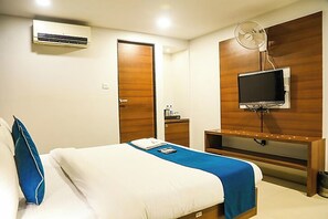 Ein Hotelzimmer mit einem Bett, einem an der Wand montierten Fernseher, einer Klimaanlage und einer Holztür.