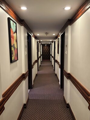 A hotel hallway with carpeted floors, wooden trim, and doors on both sides.
