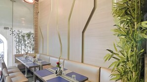 A restaurant interior with a long dining table, cushioned seating, and a large green plant. - Aboo's Hotel Concord Galaxy by Zuzu (Mumbai)