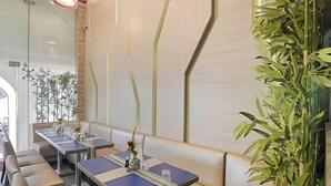L’intérieur d’un restaurant présente une longue table à manger, des sièges rembourrés et une grande plante verte.