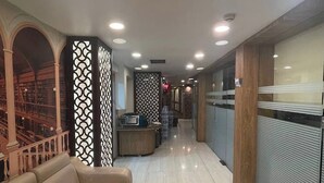 Un couloir d'hôtel avec un canapé, des paravents décoratifs, un comptoir d'accueil et un escalier.