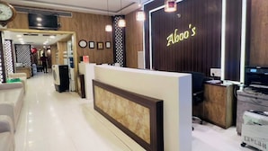 A reception area with a wooden reception desk, a clock, and a TV mounted on the wall. - Aboo's Hotel Concord Galaxy by Zuzu (Mumbai)