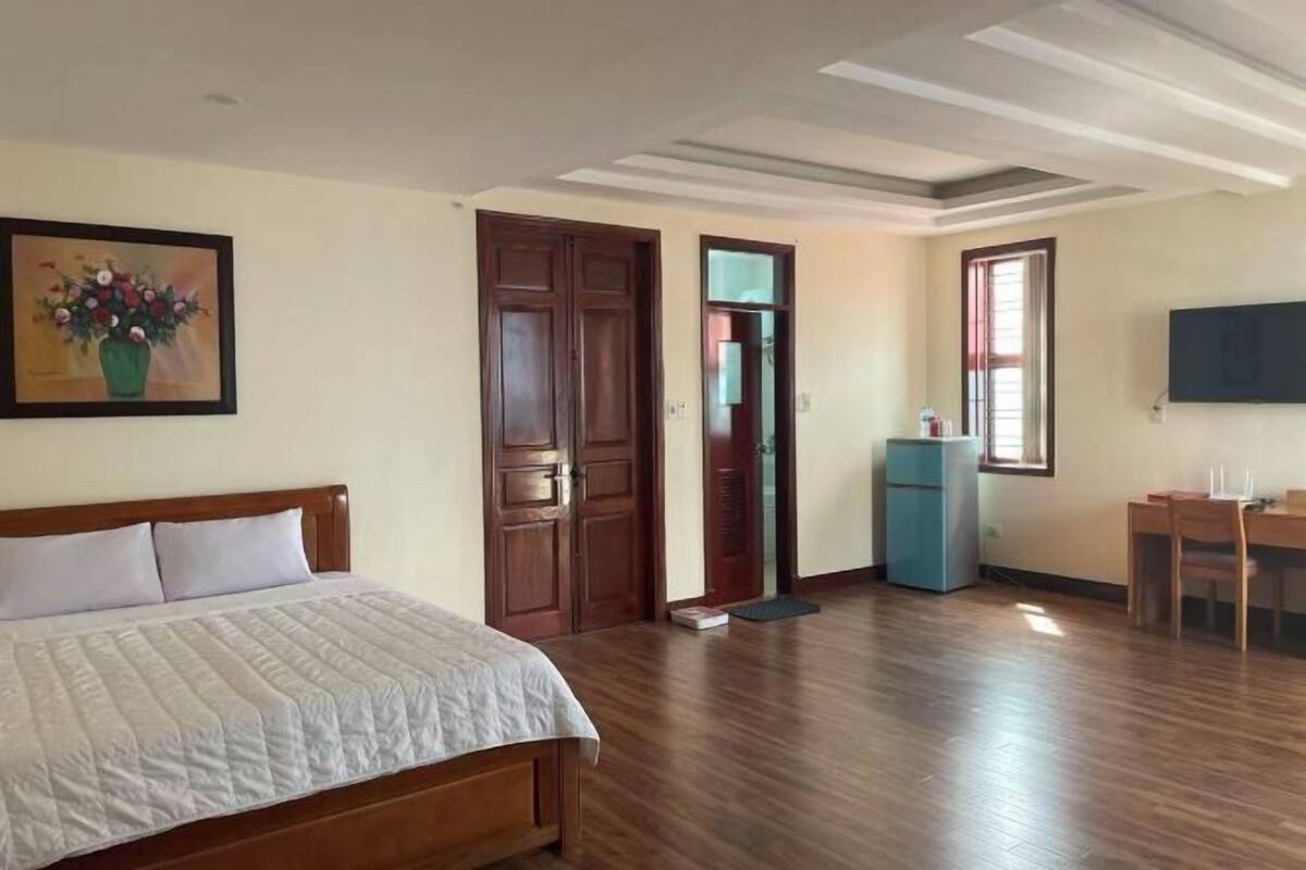 Une chambre à coucher avec un lit, une porte en bois, un petit bureau, une télévision et un tableau accroché au mur.