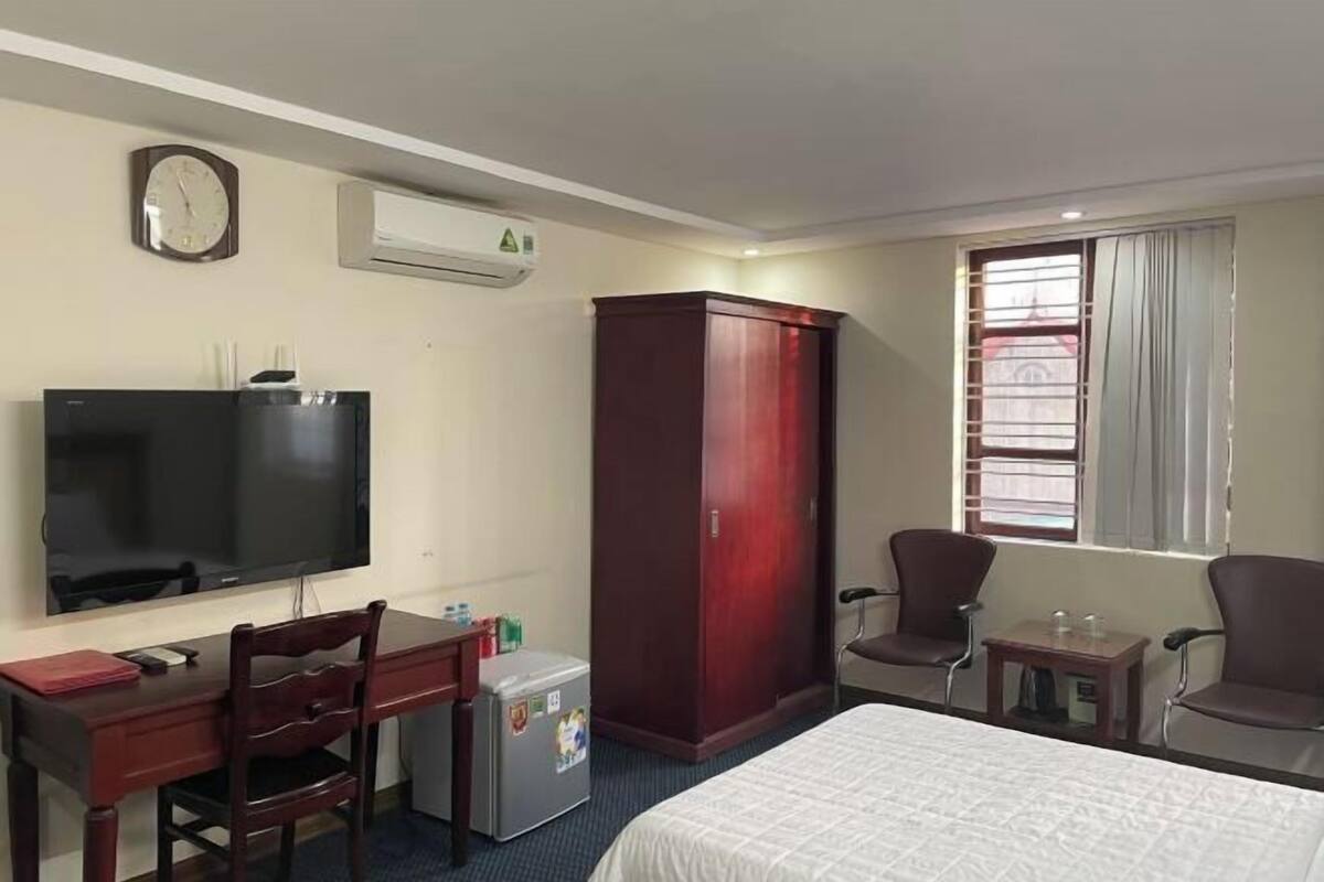 Une chambre d’hôtel comprenant un lit, un bureau avec une chaise, une télévision, une armoire et une fenêtre avec des rideaux.