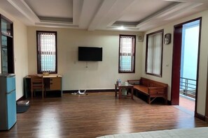 Une pièce avec un plancher en bois, un bureau avec une chaise, un téléviseur fixé au mur et une fenêtre donnant sur un beau paysage.