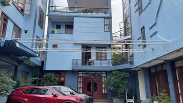 A multi-story residential building with a blue facade, balconies, and a red car parked in the driveway.