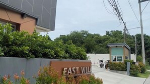 Señal de 'East Village' con un edificio moderno al fondo, una pequeña estructura con una persona y cielo despejado.
