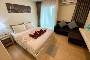 A hotel room with a bed, a sofa, a desk, and a window with curtains. - Sunrise good view @ East Ville Bangsaen (Chon Buri)