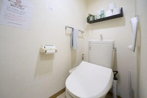 Een badkamer met toilet, een plank met toiletartikelen en een papiersbord aan de muur.