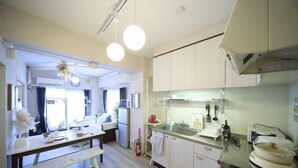 A compact kitchen with white cabinets, a microwave, a sink, and a stove. There is a dining table with chairs and a bench. - Mezon Etowaru #706 (Nagoya)